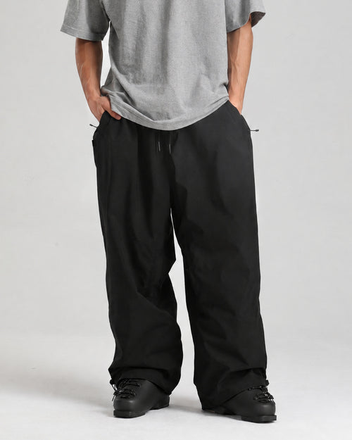 NOJU Core 2L baggy ski pants in black, front view, worn with black ski boots