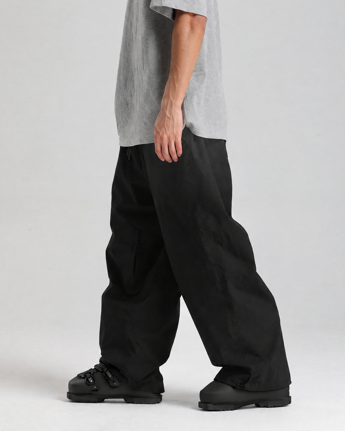 NOJU Core 2L baggy ski pants in black, side view showing the baggy fit, worn with black ski boots