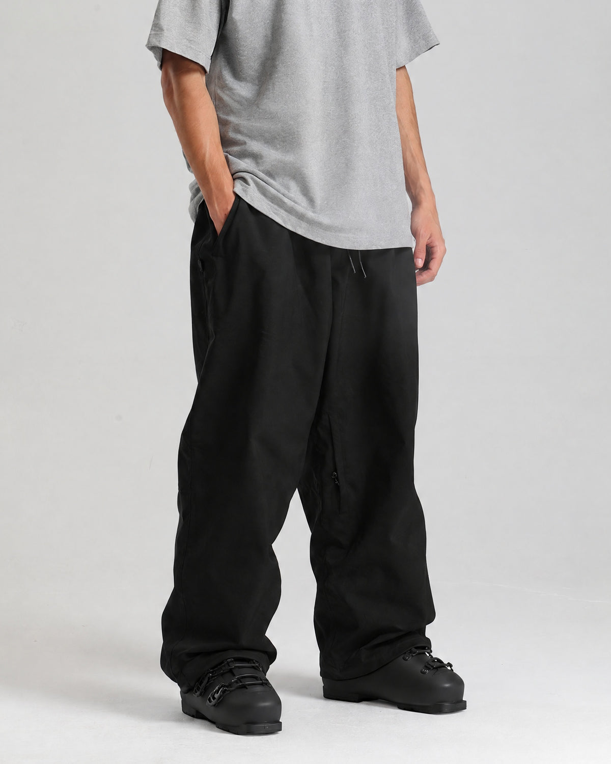 NOJU Core 2L baggy ski pants in black, three-quarter view showing the wide leg, worn with black ski boots