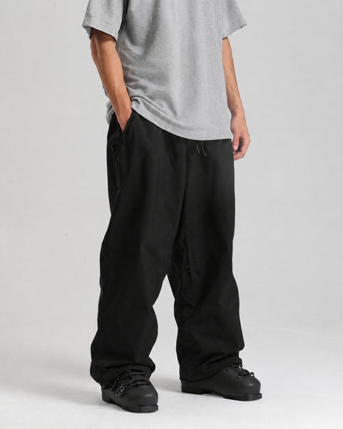 NOJU Core 2L baggy ski pants in black, three-quarter view showing the wide leg, worn with black ski boots