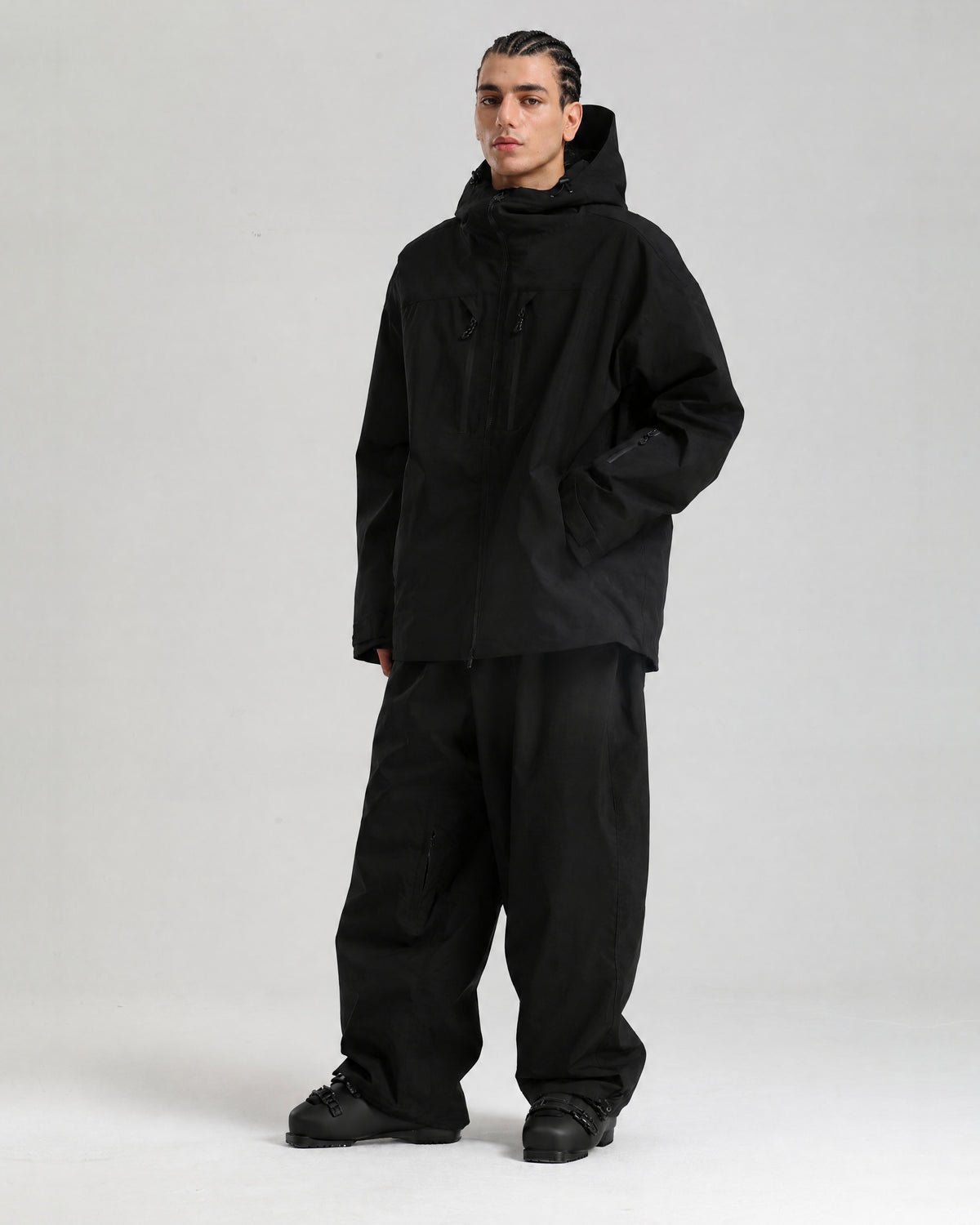 NOJU Core 2L insulated ski jacket in black, full-length three-quarter view with black baggy ski pants and ski boots